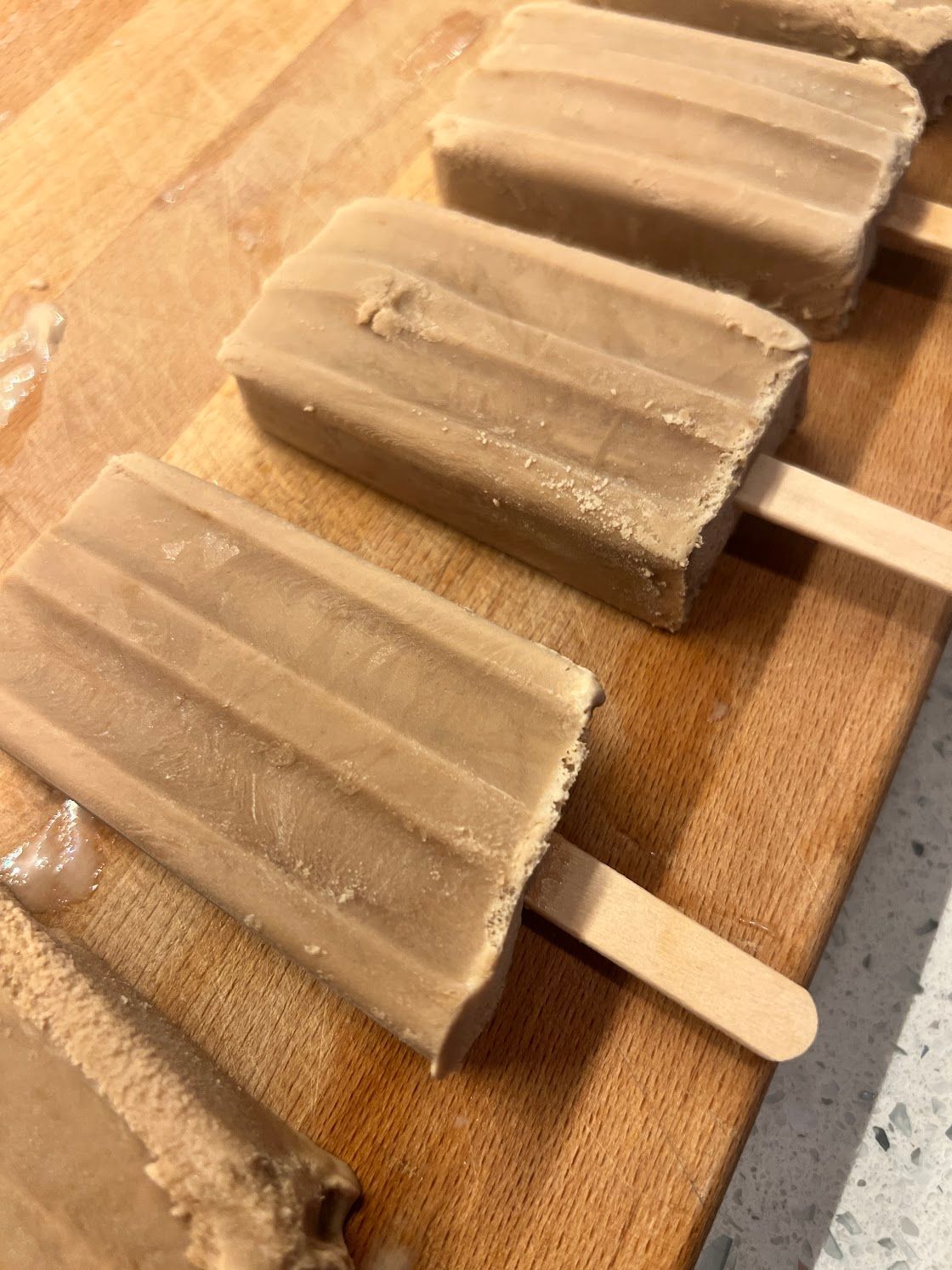 Three popsicles are sitting on a wooden cutting board.