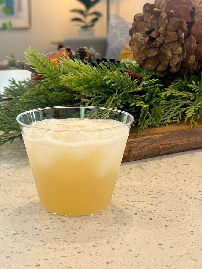 A cup of liquid is sitting on a counter next to pine cones.