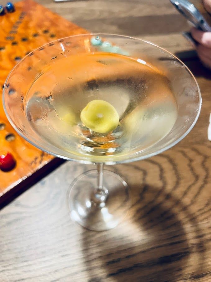 A martini with a green olive in it is on a wooden table.