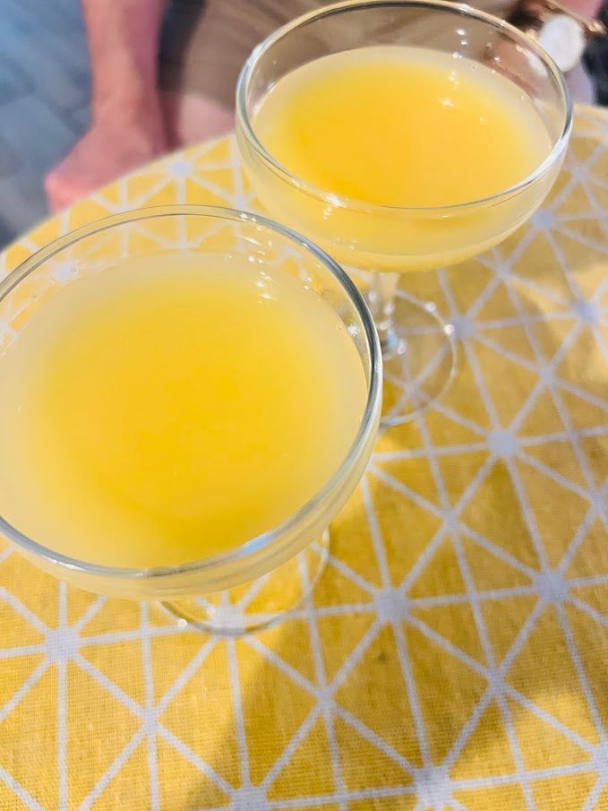 Two glasses of yellow liquid are sitting on a table.