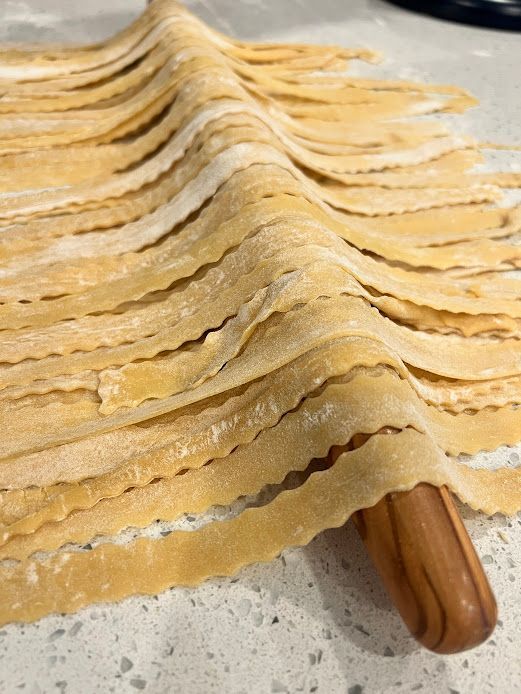 A wooden rolling pin is sitting on top of a pile of noodles.