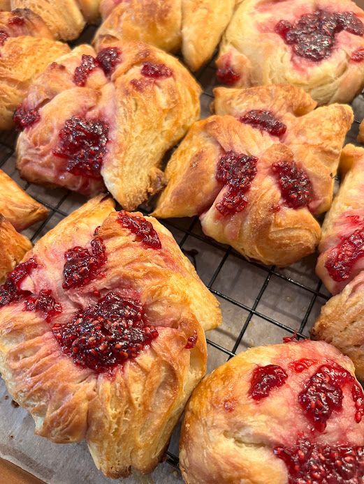 A bunch of pastries with raspberries on them are sitting on a cooling rack.