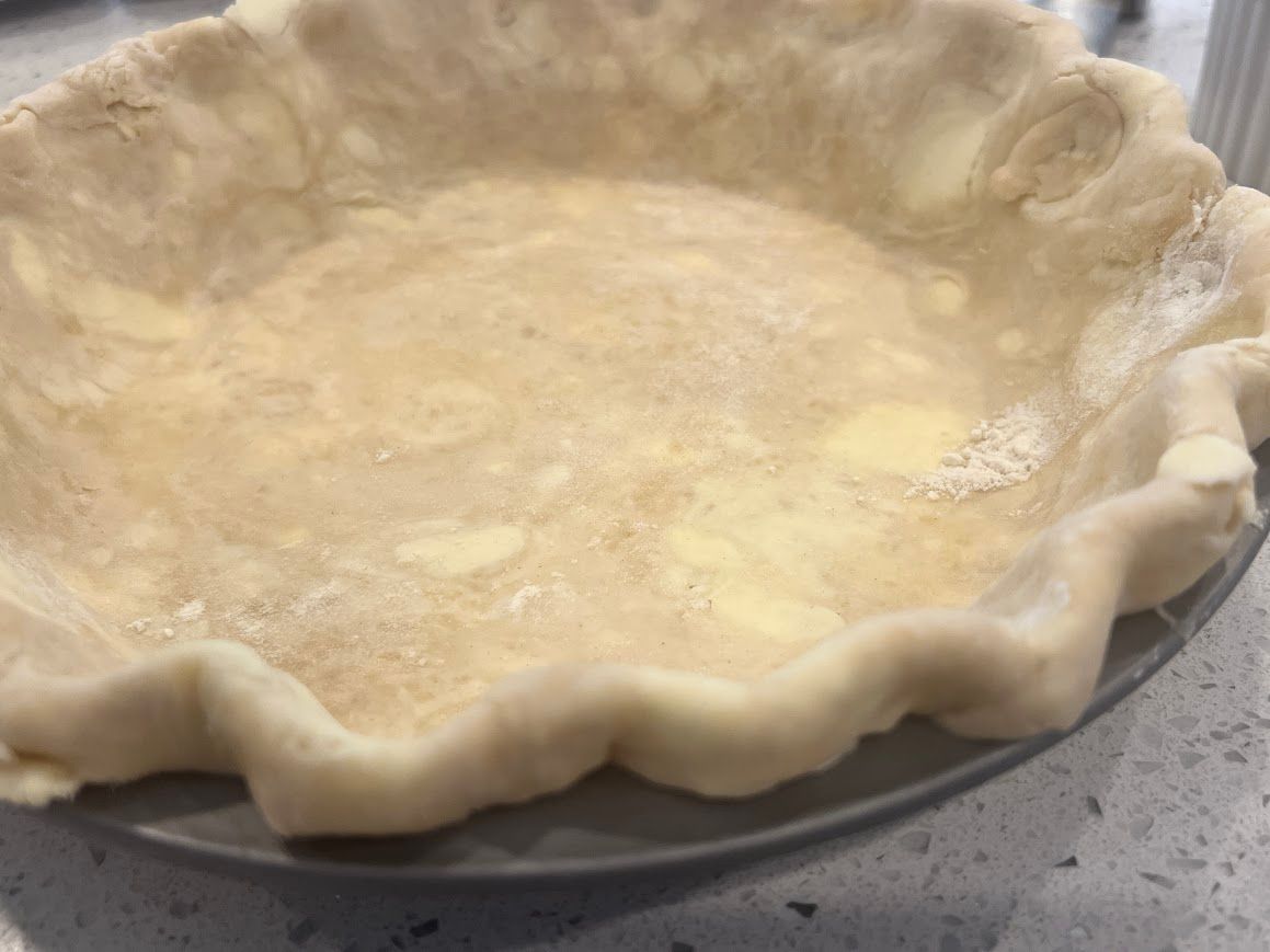 A pie crust is sitting on top of a pie pan on a counter.