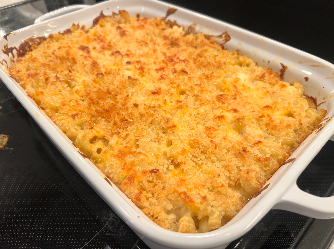 A white casserole dish filled with macaroni and cheese is sitting on top of a stove.