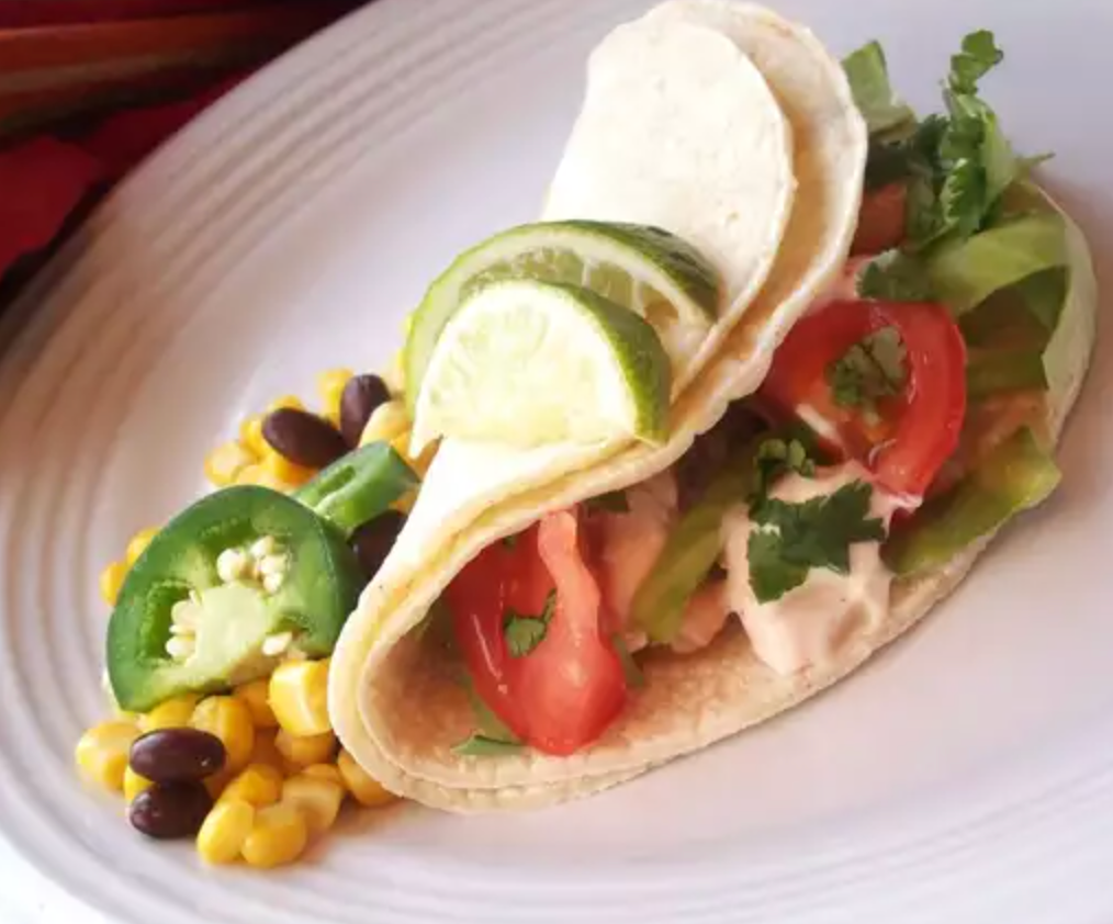 A taco with tomatoes jalapenos corn and black beans on a white plate