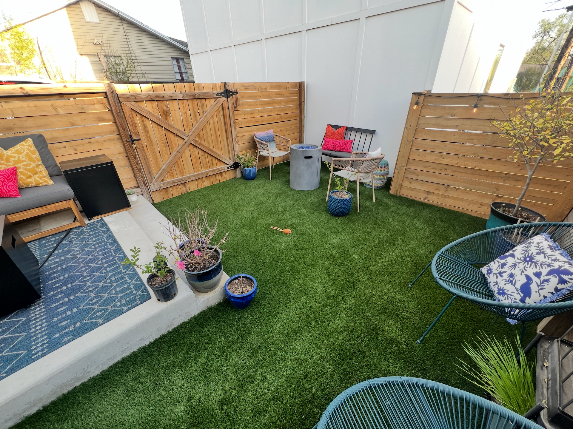 A backyard with a fence , chairs , a table and potted plants.