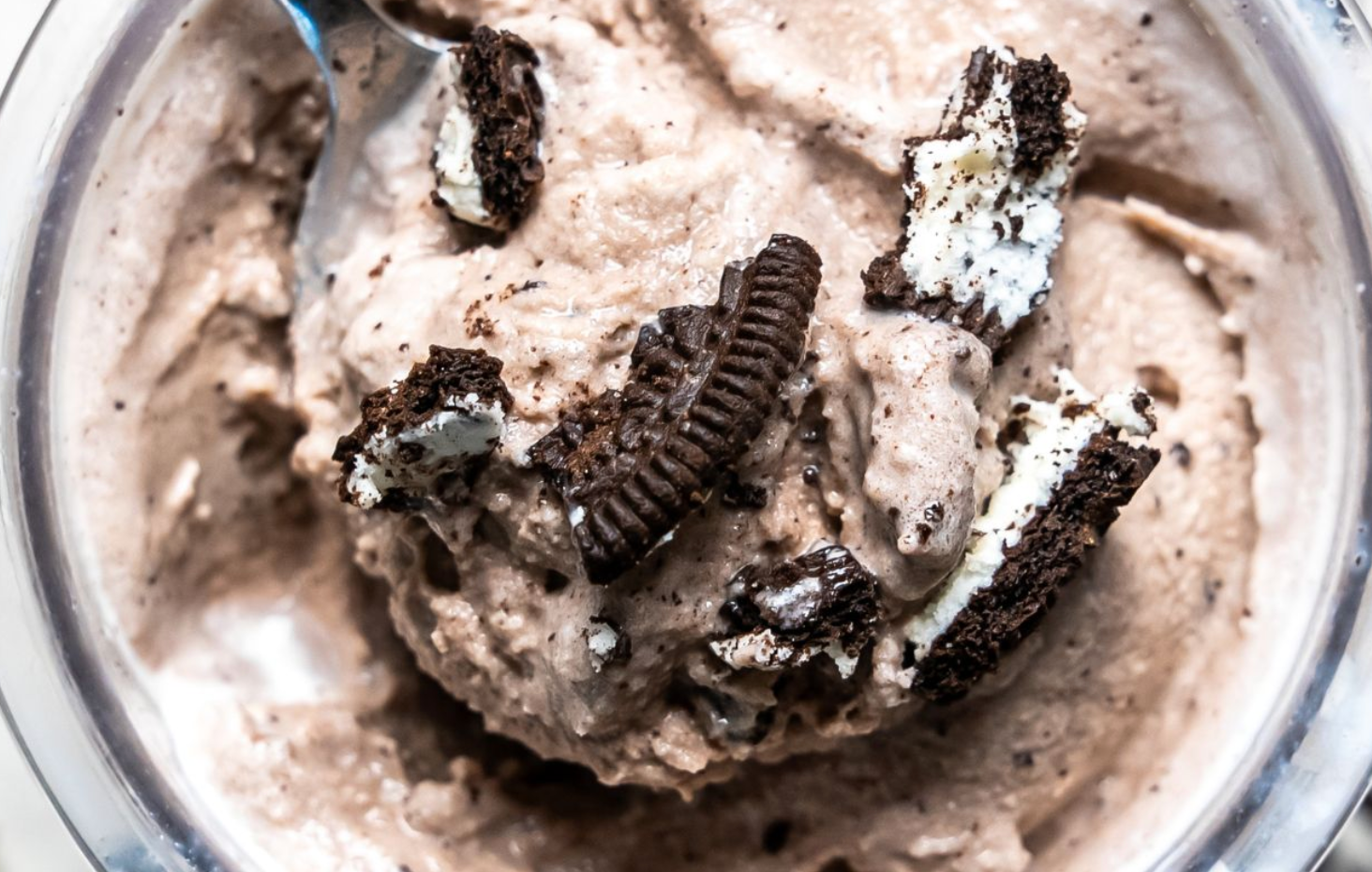 A bowl of chocolate ice cream with oreos and a spoon in it.