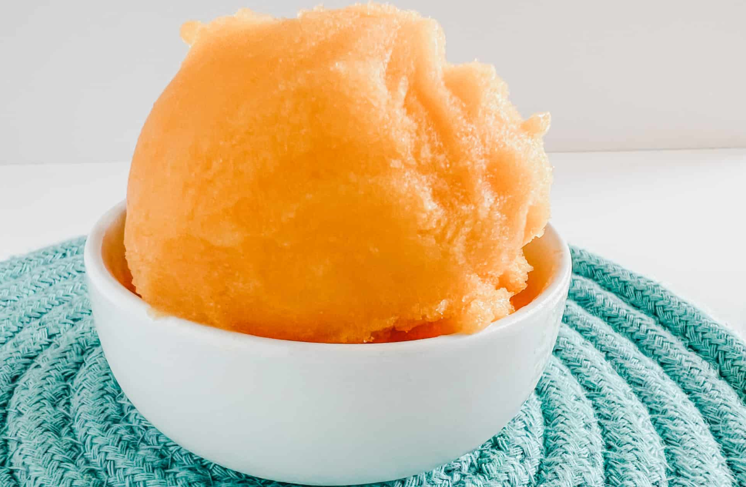 A bowl of orange ice cream is sitting on a blue towel.