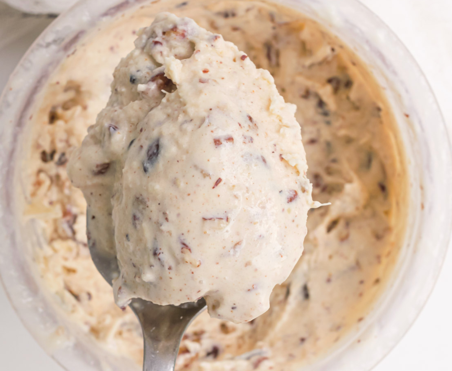 A spoon is holding a scoop of ice cream over a bowl of ice cream.