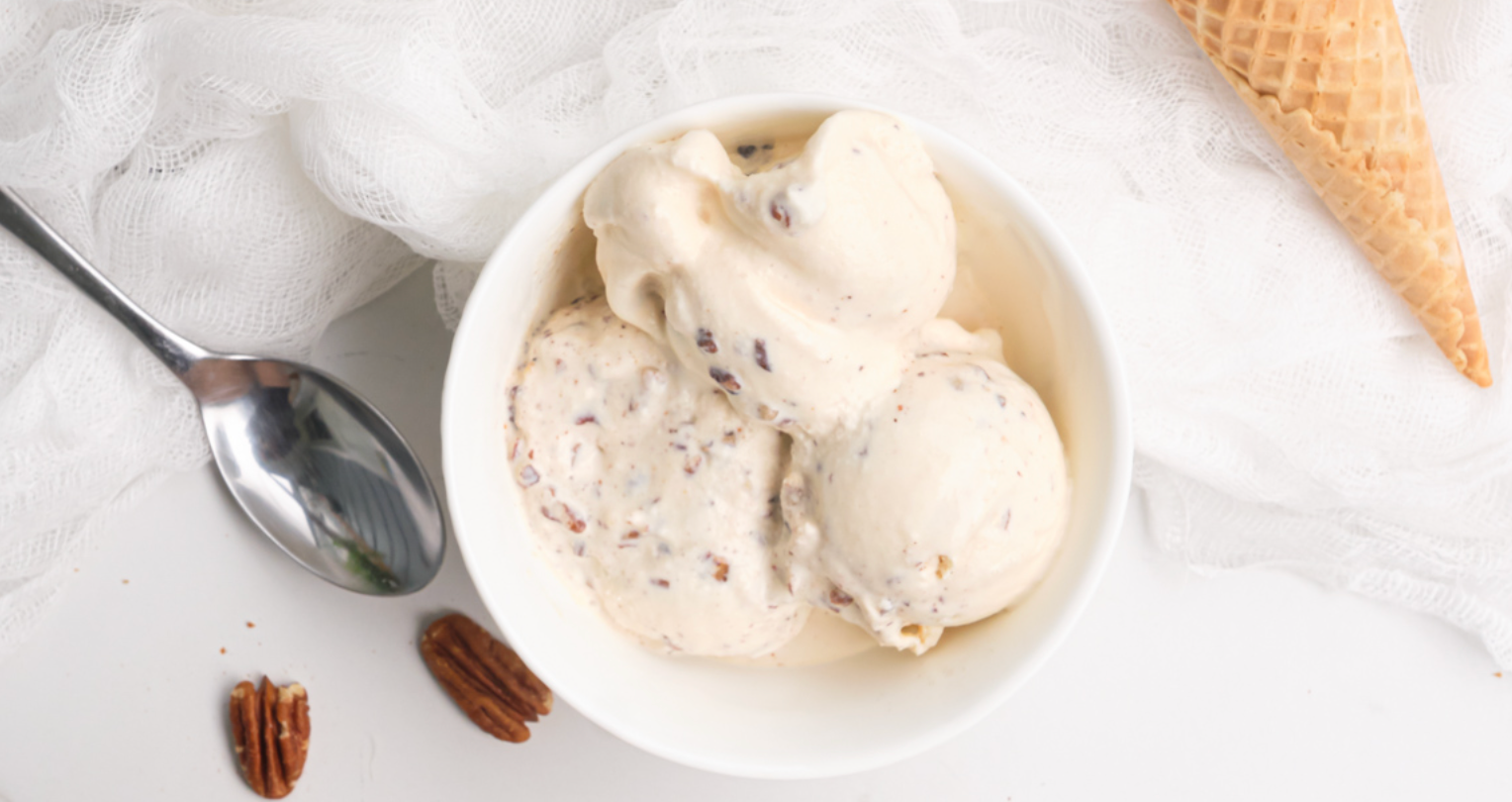 A bowl of pecan ice cream next to a waffle cone and a spoon.