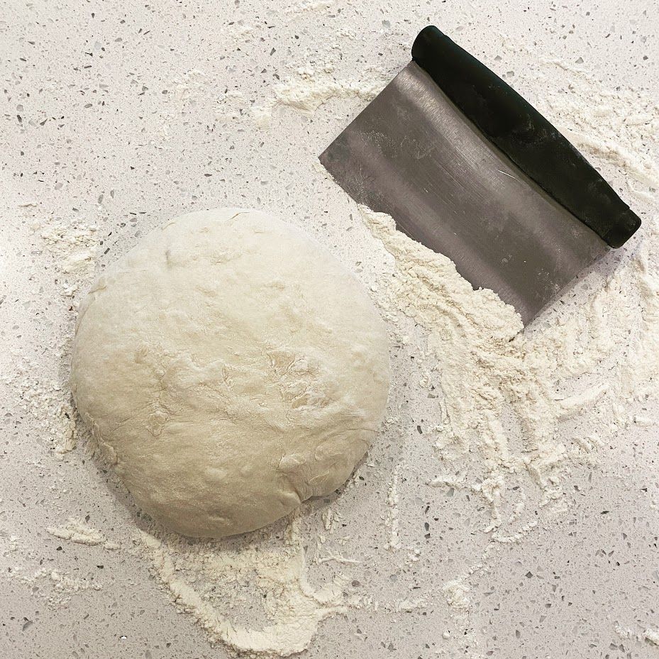 A ball of dough sits on a counter next to a spatula