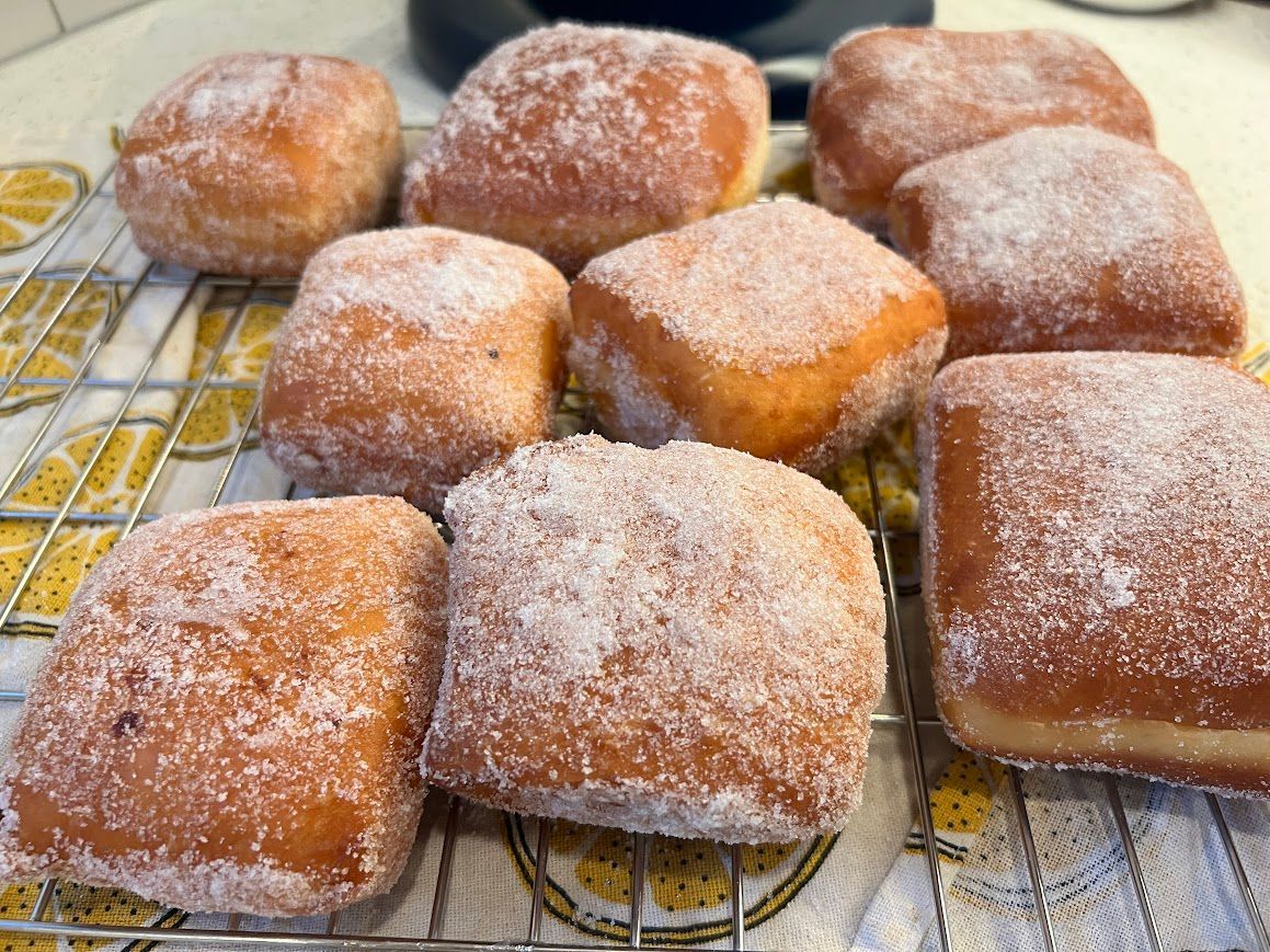 A bunch of doughnuts are sitting on a cooling rack covered in powdered sugar.