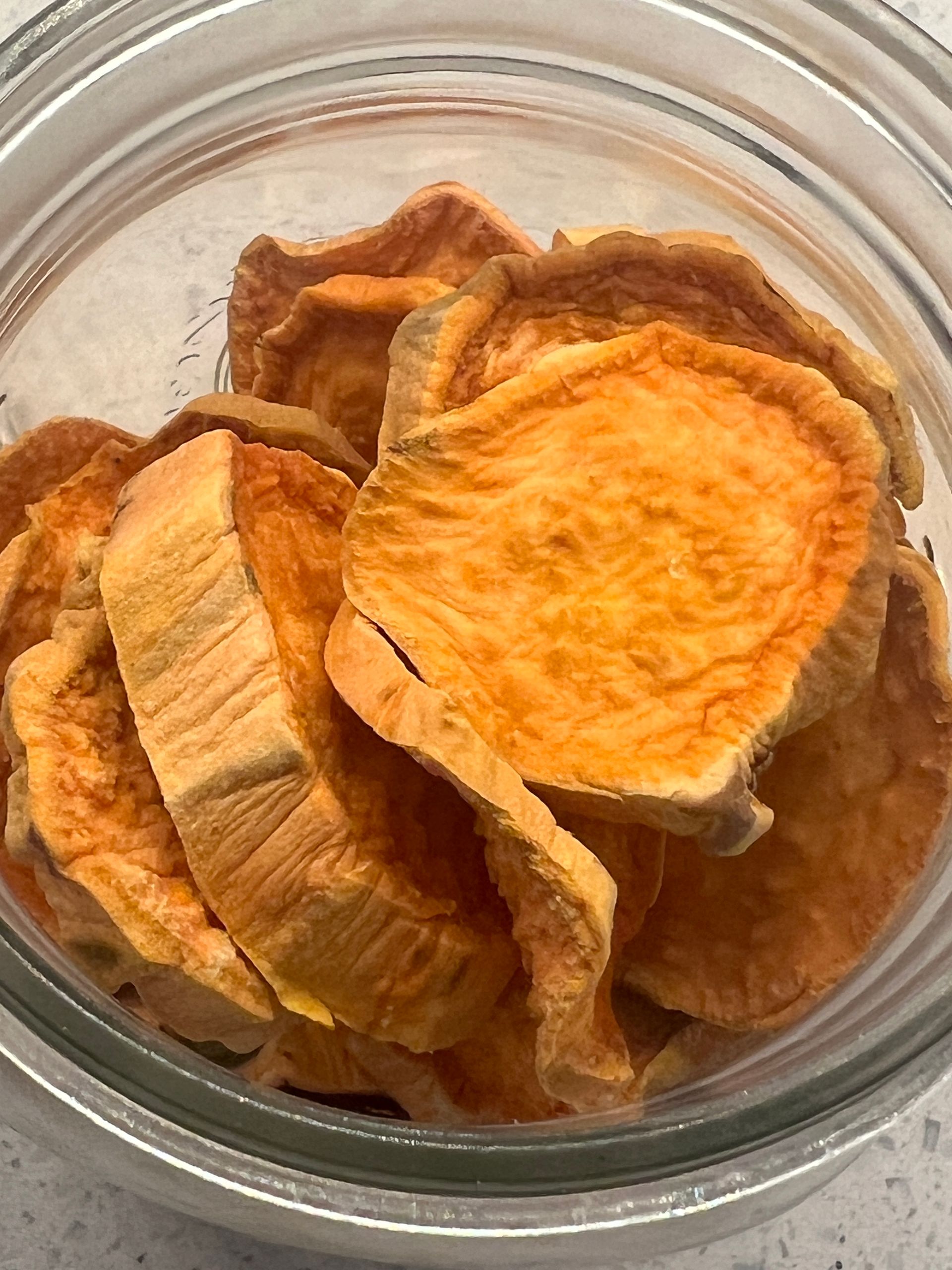 A glass bowl filled with dried sweet potato chips on a table.