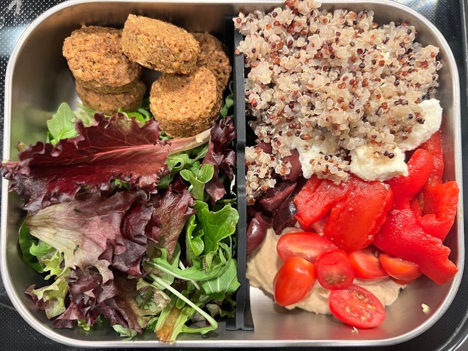 A stainless steel lunch box filled with rice , vegetables and falafel.