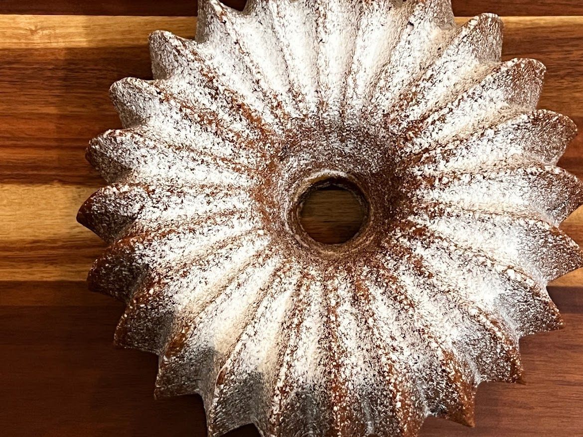 A bundt cake covered in powdered sugar is sitting on a wooden cutting board.