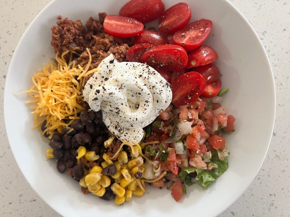 A bowl of food with tomatoes , corn , black beans , cheese and sour cream.