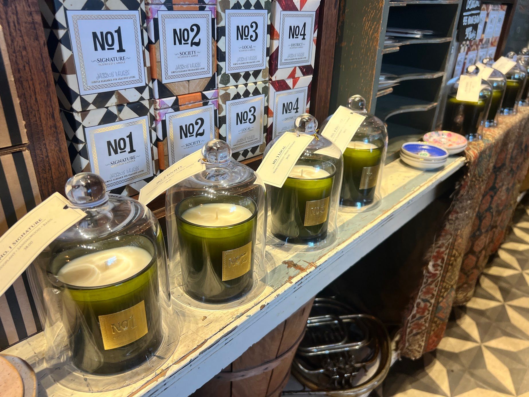 A row of candles in glass jars on a shelf in a store.