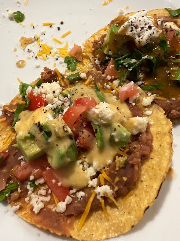 A close up of two tacos with beans , tomatoes , cheese and guacamole on a white plate.