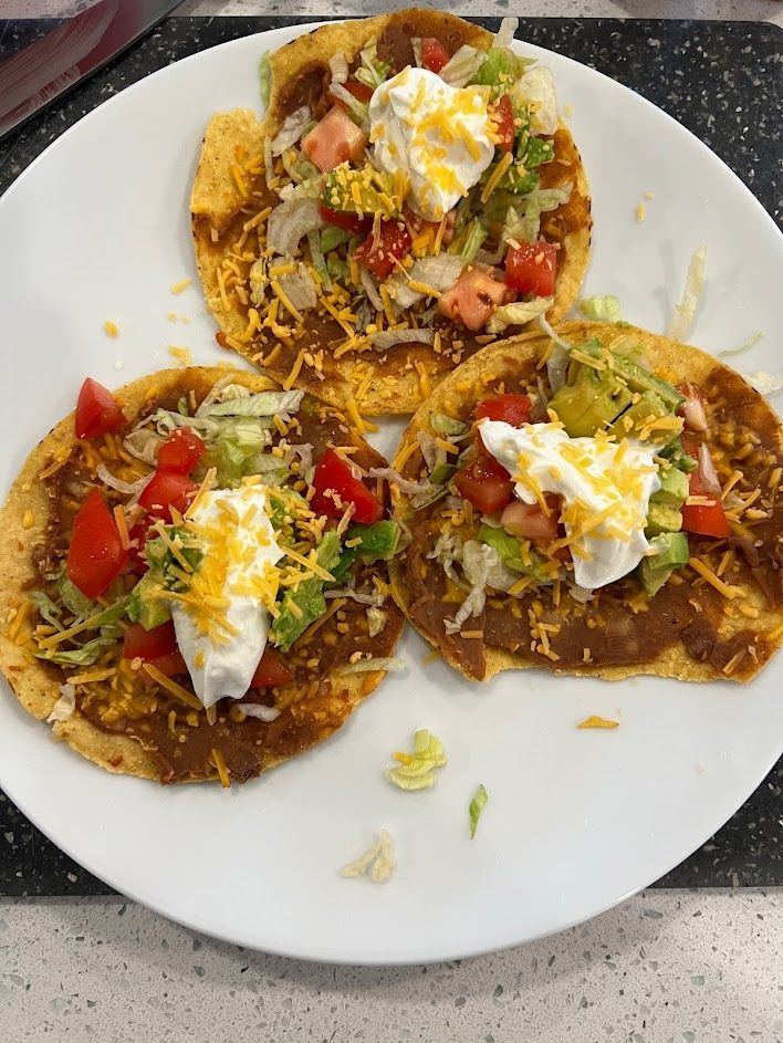 A white plate topped with three tacos with beans , cheese , tomatoes and lettuce.