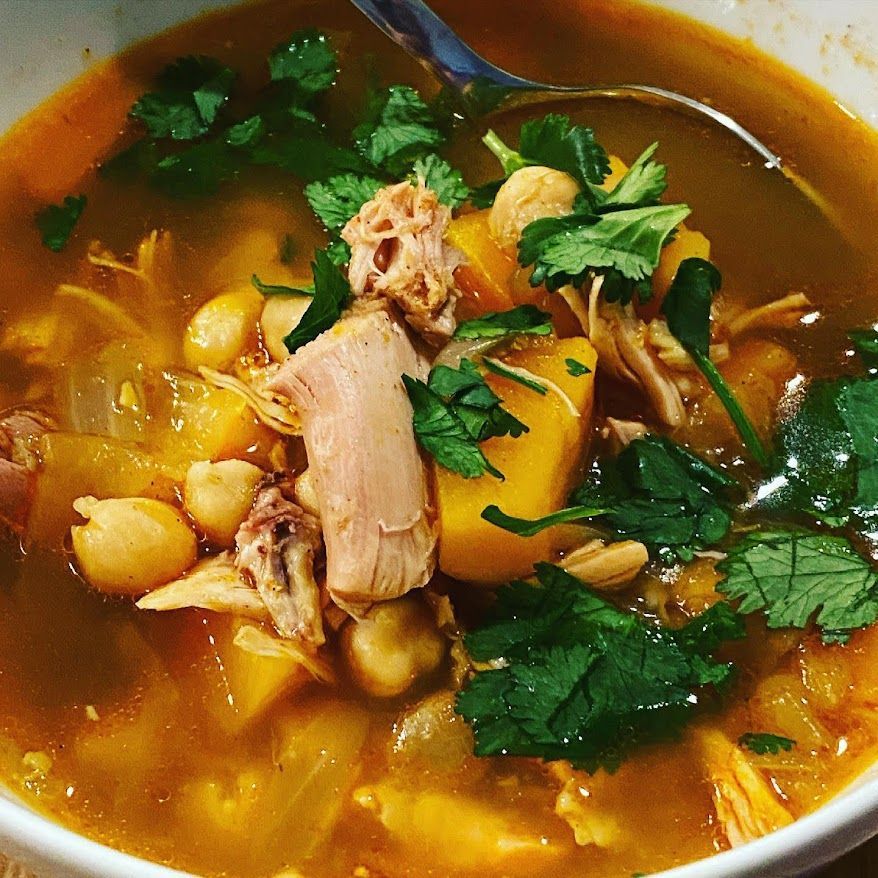 A bowl of soup with chicken chickpeas and potatoes with a spoon in it