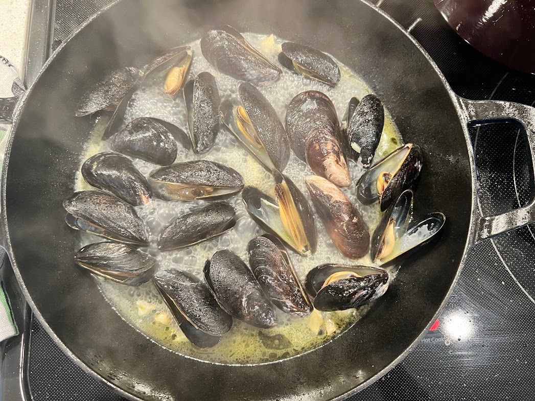 Mussels are being cooked in a pan on a stove.