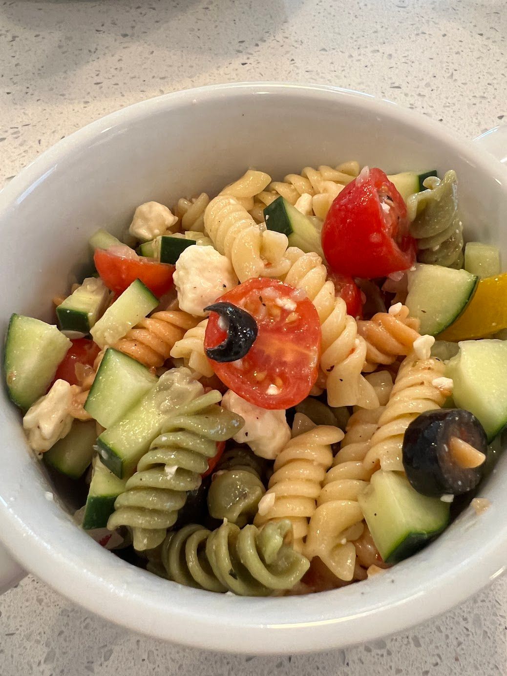 A pasta salad with tomatoes , cucumbers , olives and feta cheese