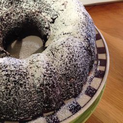 A close up of a chocolate bundt cake covered in powdered sugar on a plate.