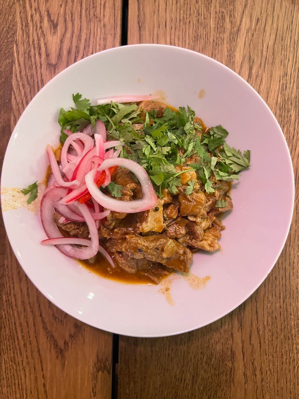 A white plate topped with meat and onions on a wooden table.