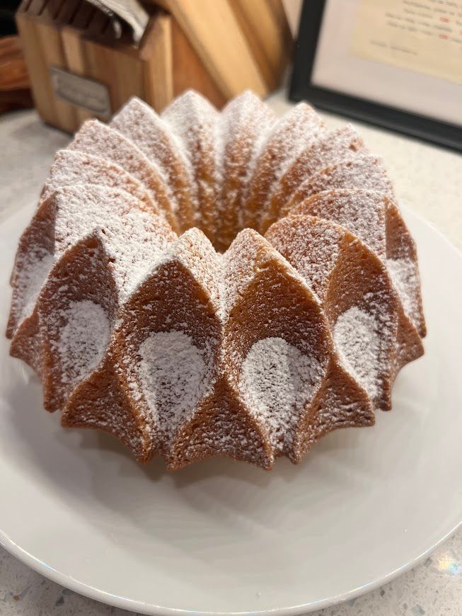 A bundt cake with powdered sugar on top is on a white plate.