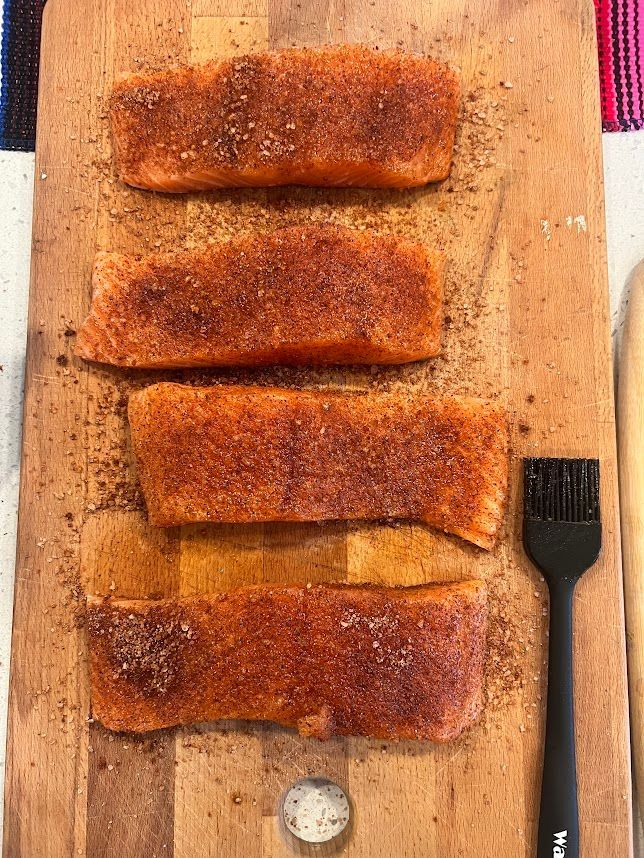 A wooden cutting board topped with slices of salmon and a brush.