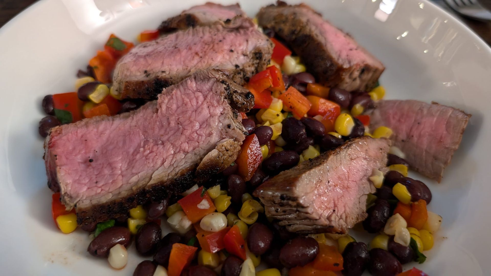 A white plate topped with steak , black beans , corn and peppers.