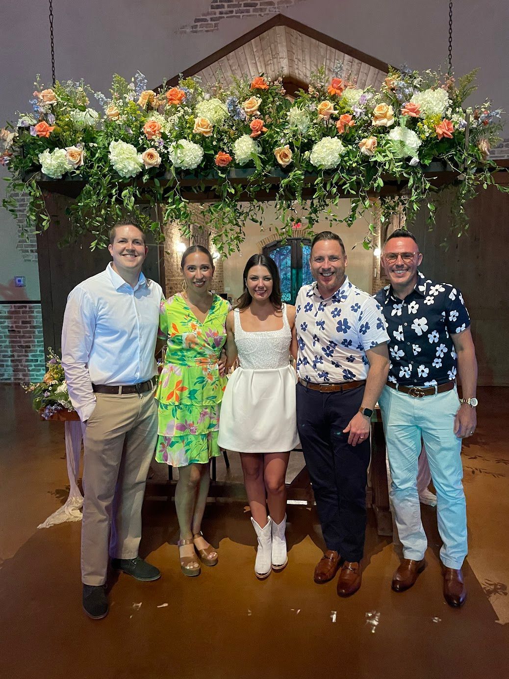 A group of people are posing for a picture in front of a floral arch.