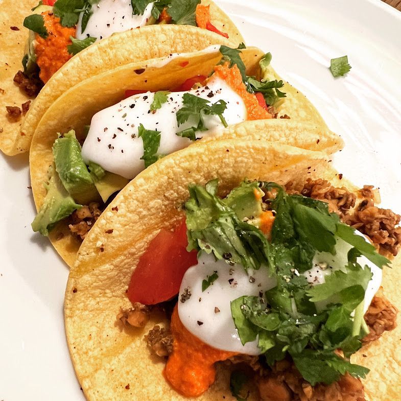 A white plate topped with three tacos with meat and vegetables