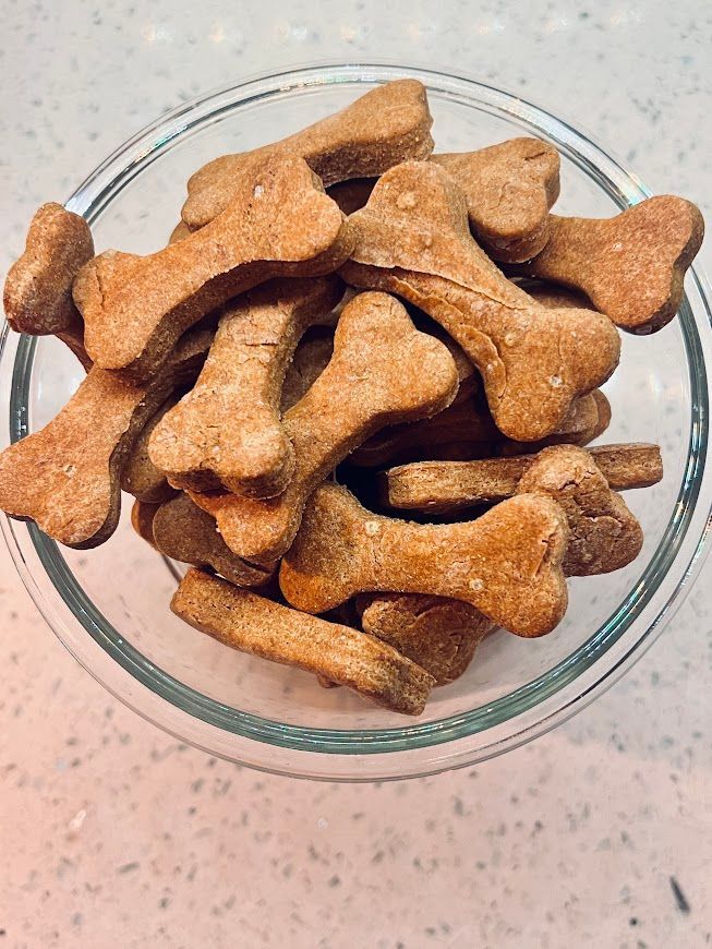 A glass bowl filled with dog treats in the shape of bones.