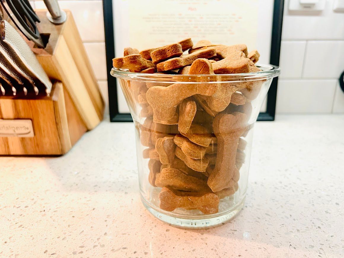 A glass filled with dog treats is sitting on a counter.