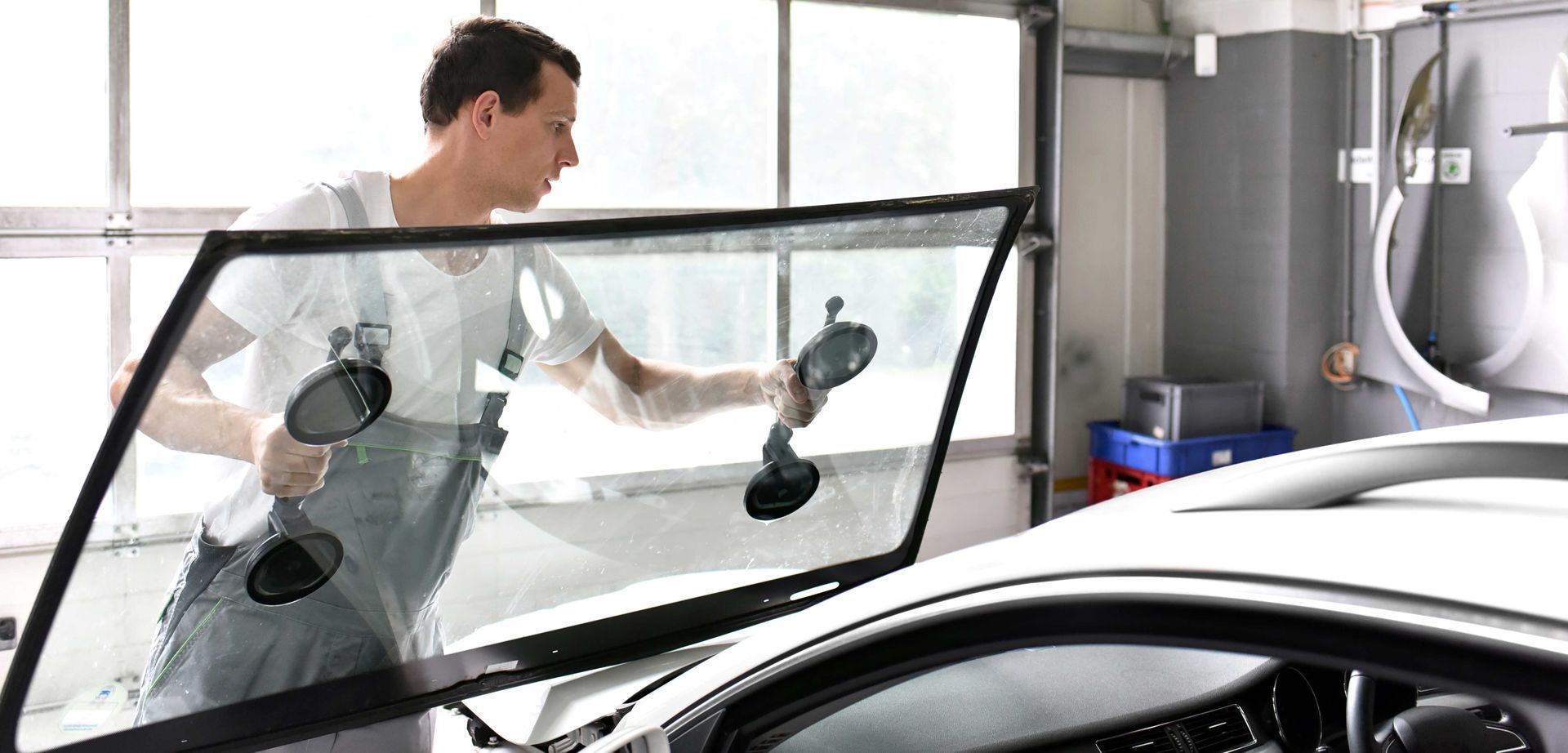 A man is installing a windshield on a car in a garage.