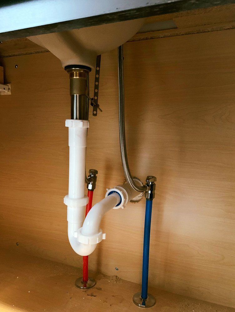 Under-sink plumbing with white drain pipe, red and blue water lines, and a flexible supply hose.