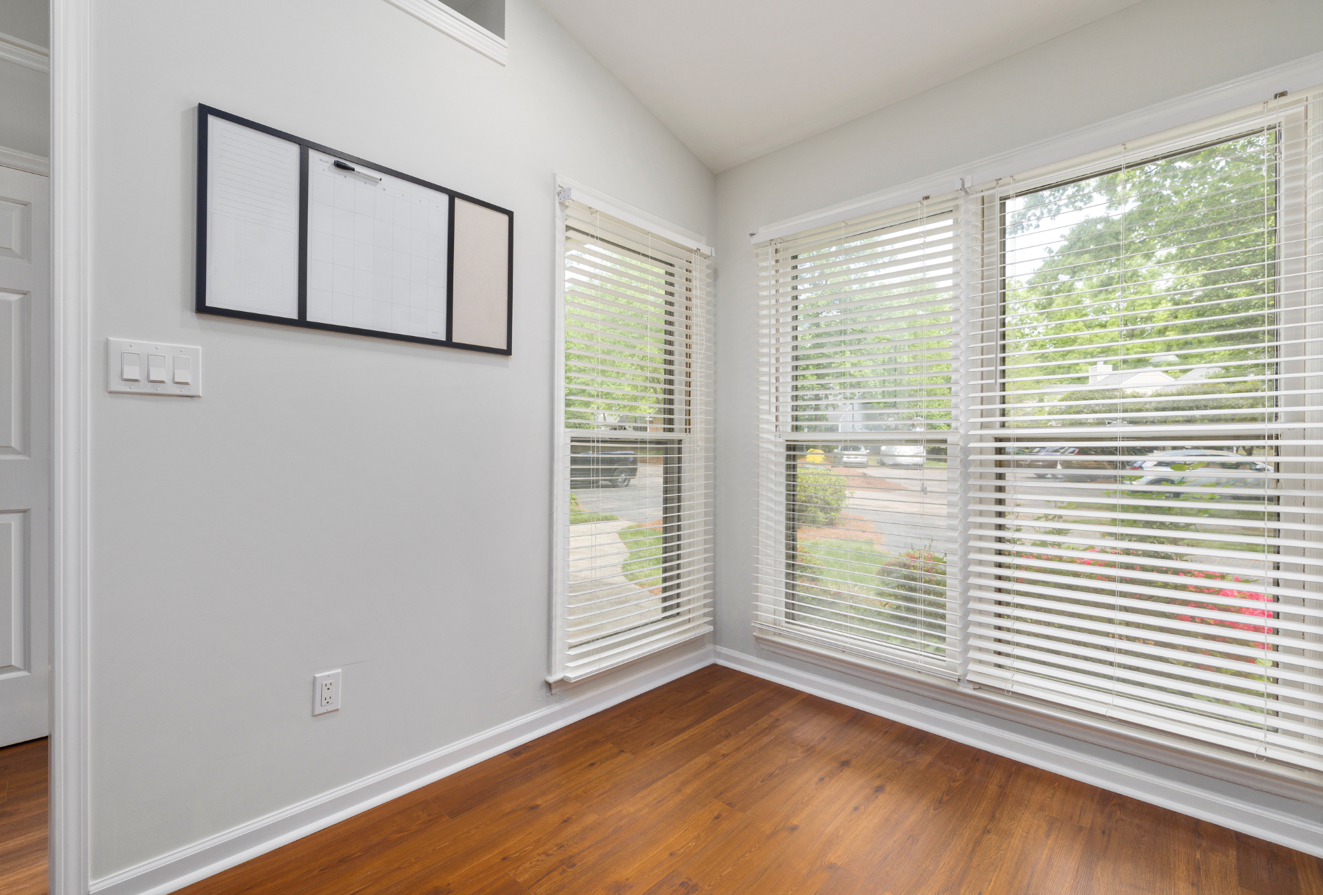An empty room with hardwood floors , white blinds , and a large window.