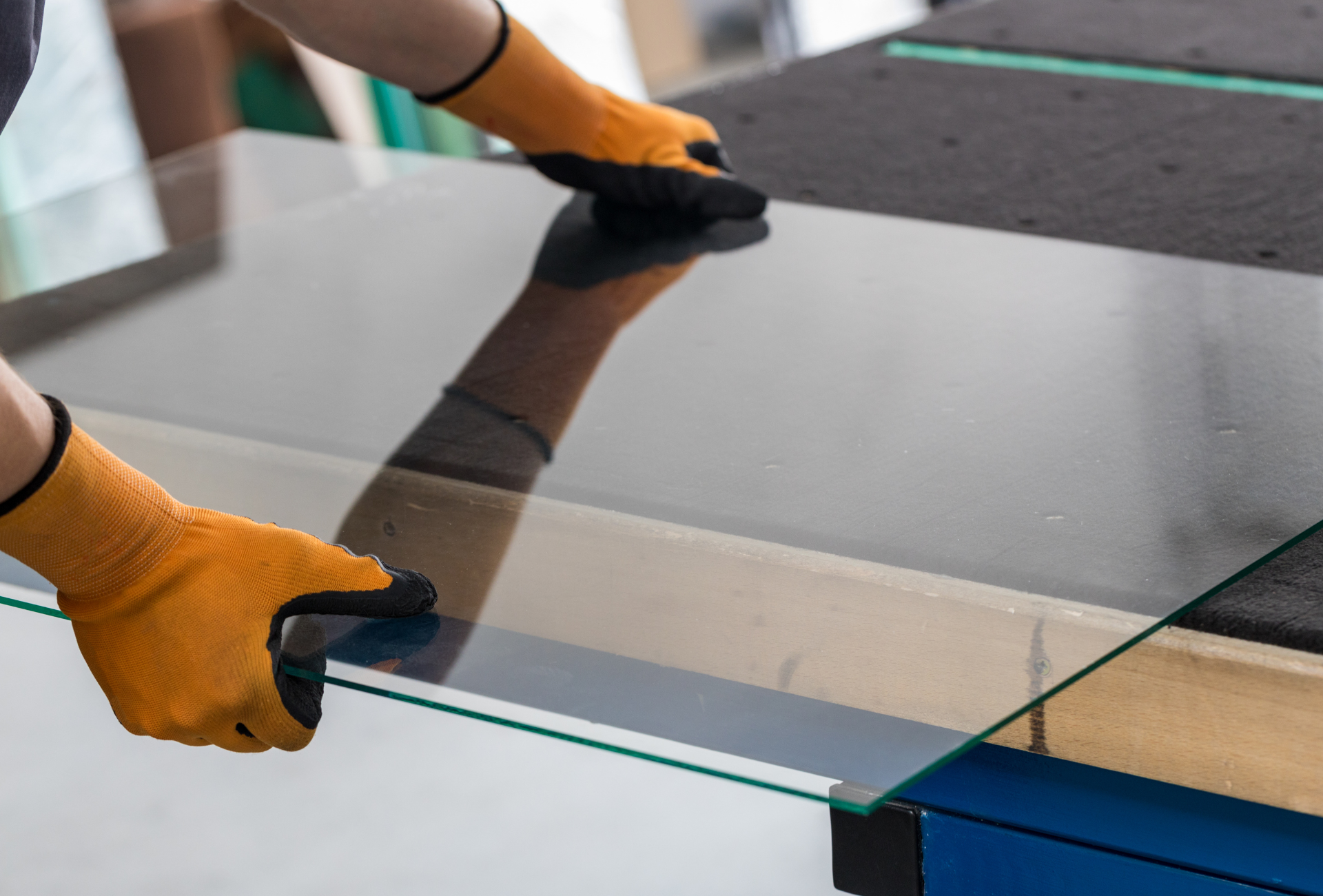A person wearing orange gloves is cutting a piece of glass