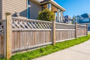 A wooden fence along a sidewalk in front of a house.