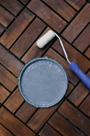 A can of paint and a paint roller are on a wooden table.