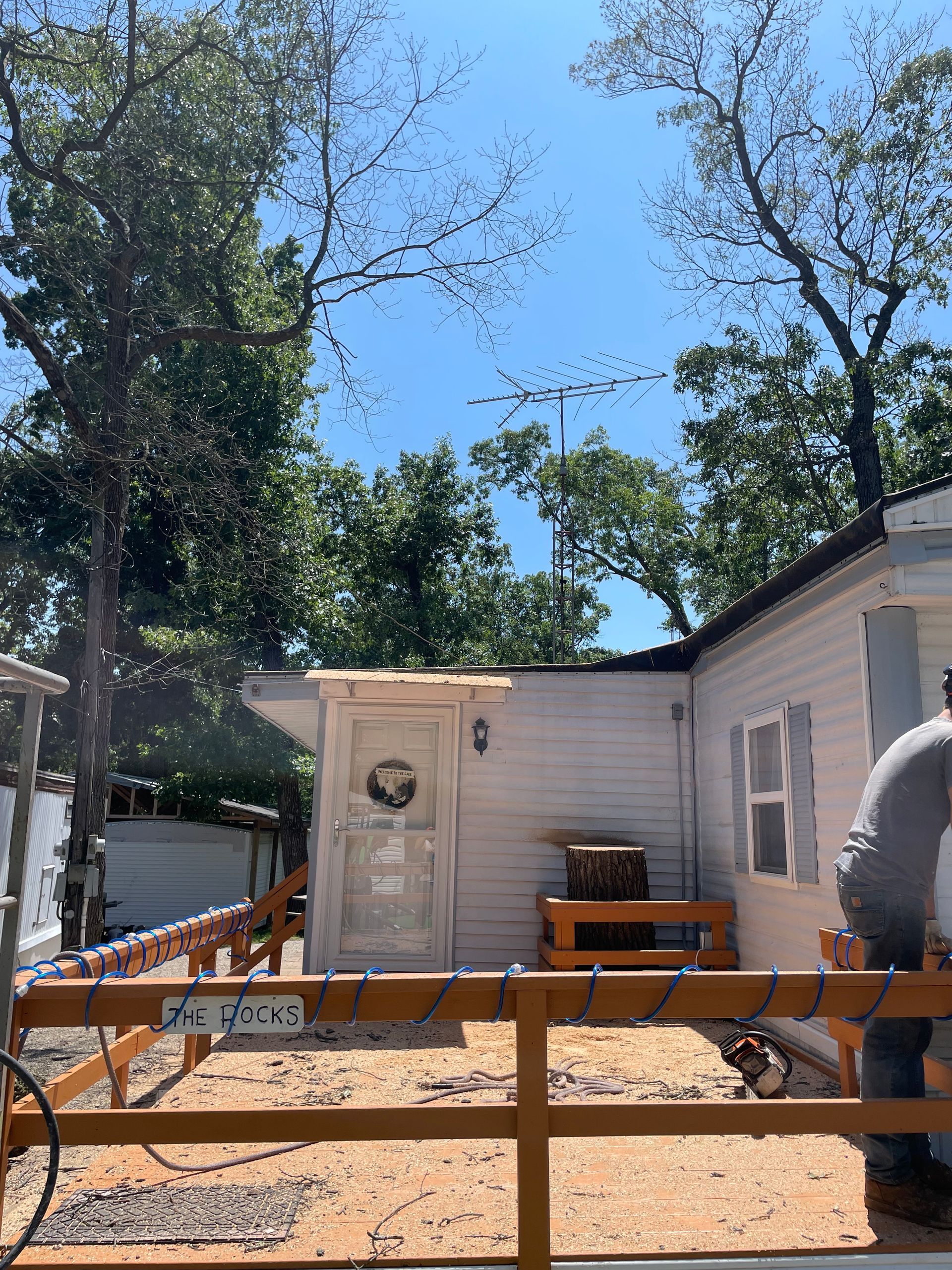 A man is working on a wooden fence in front of a mobile home.