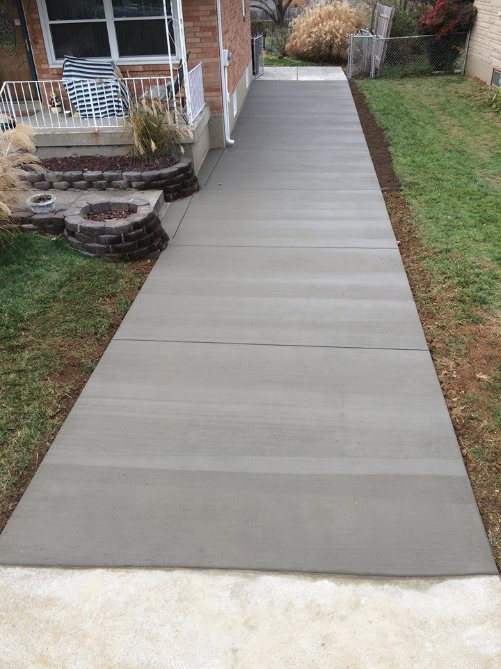 A concrete walkway leading to a house with a fire pit in the backyard.