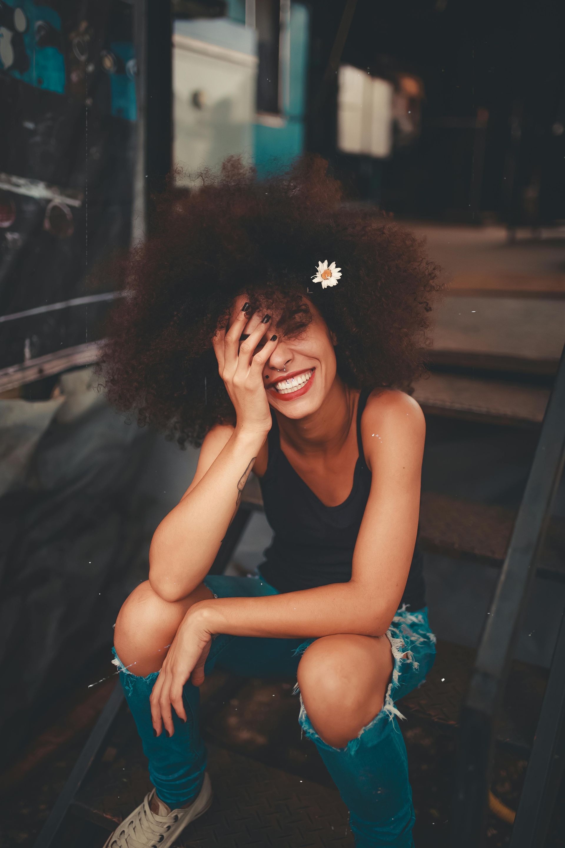 A woman with an afro is sitting on a set of stairs covering her face with her hand.