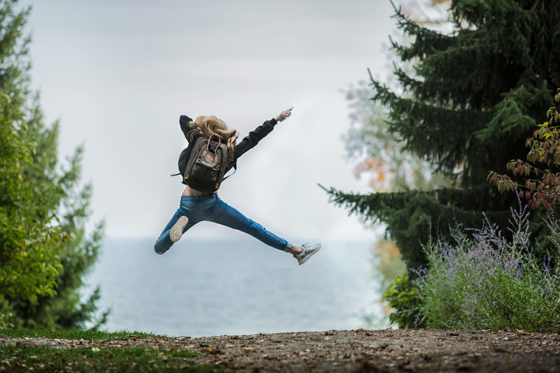 A woman with a backpack is jumping in the air.