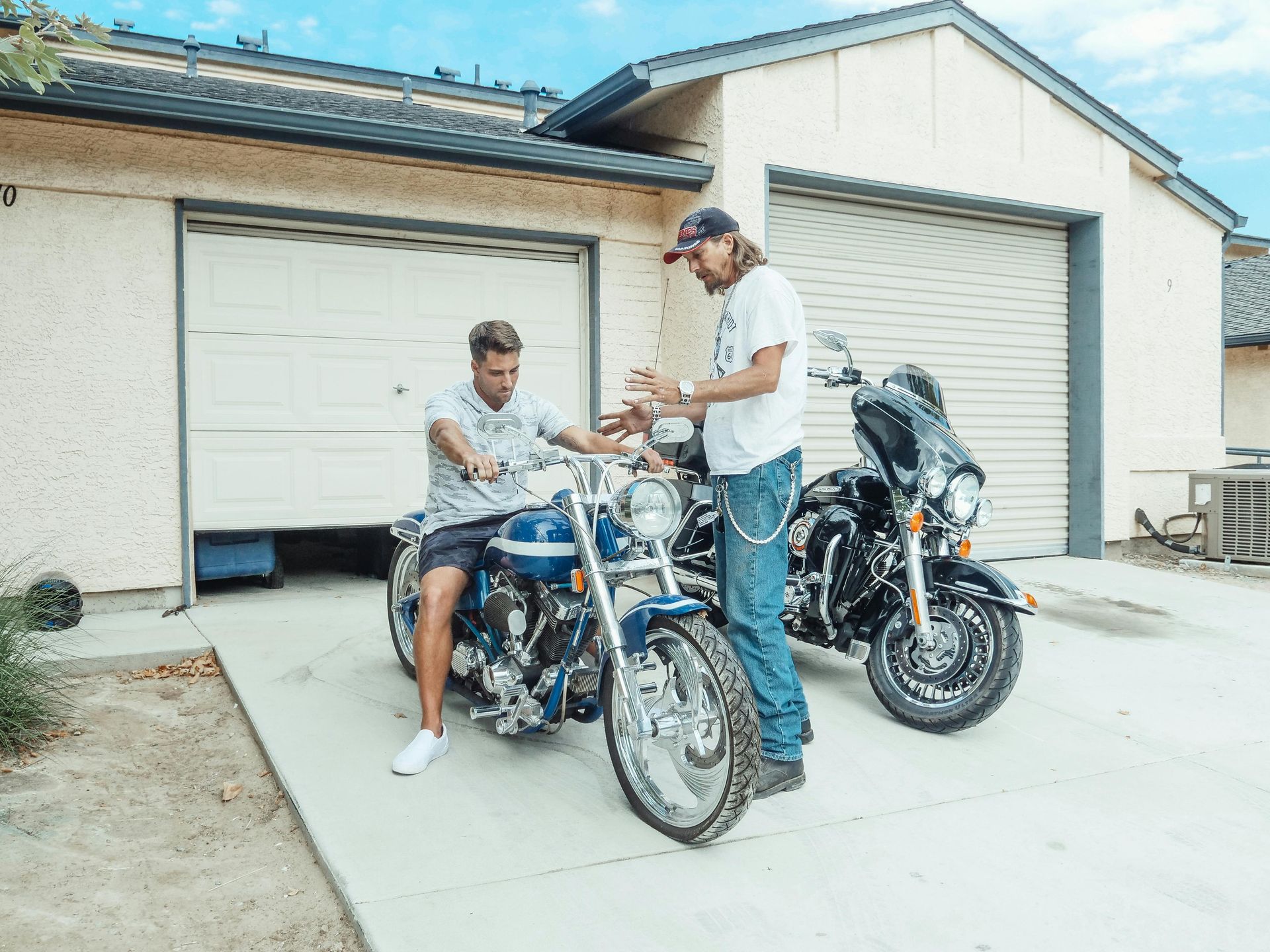 A man and a boy are standing next to a motorcycle in front of a garage.