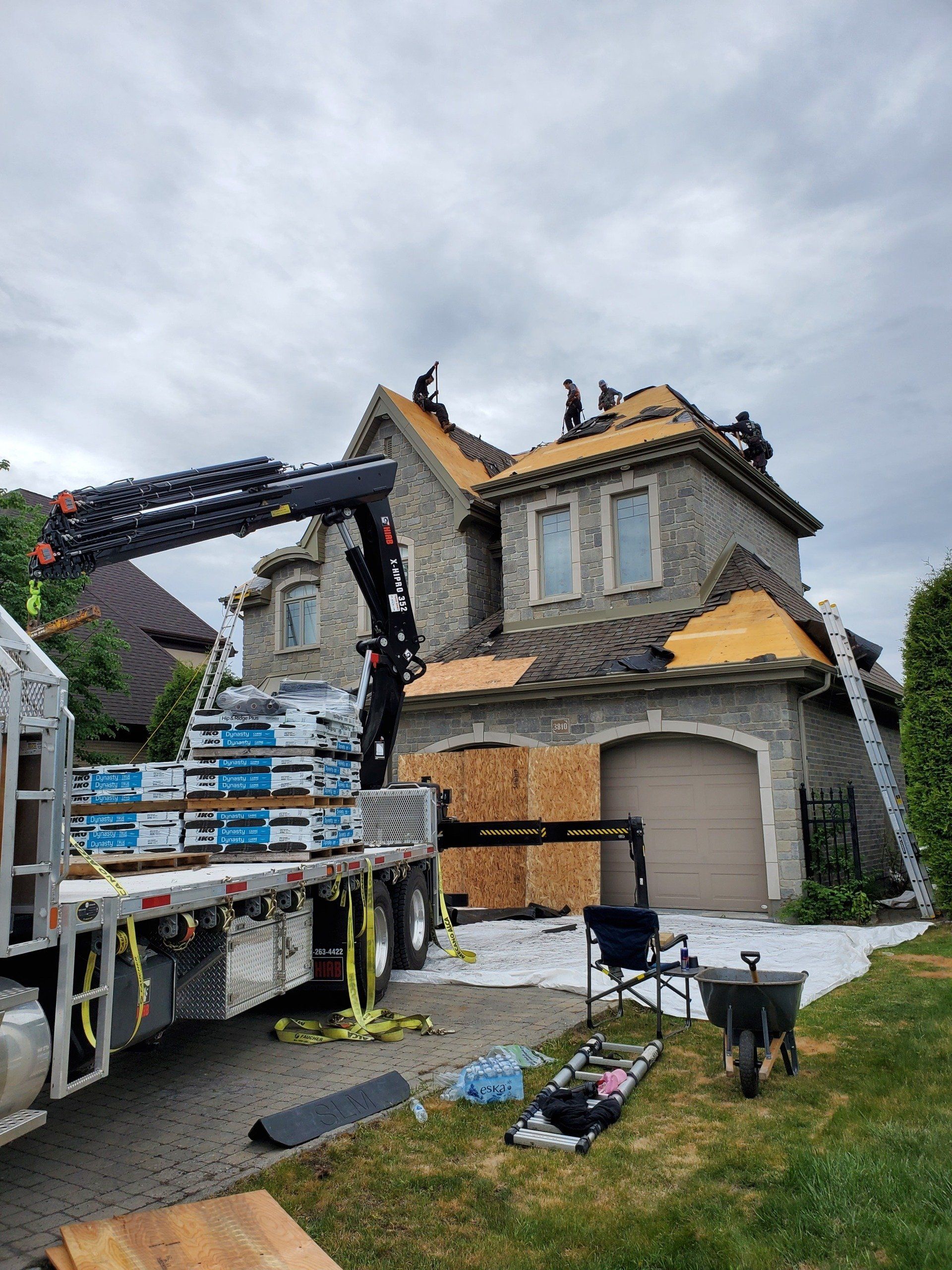 Four guys are roofing one house. There is also a container of roofing materials, which is beside the home, to support the operation.