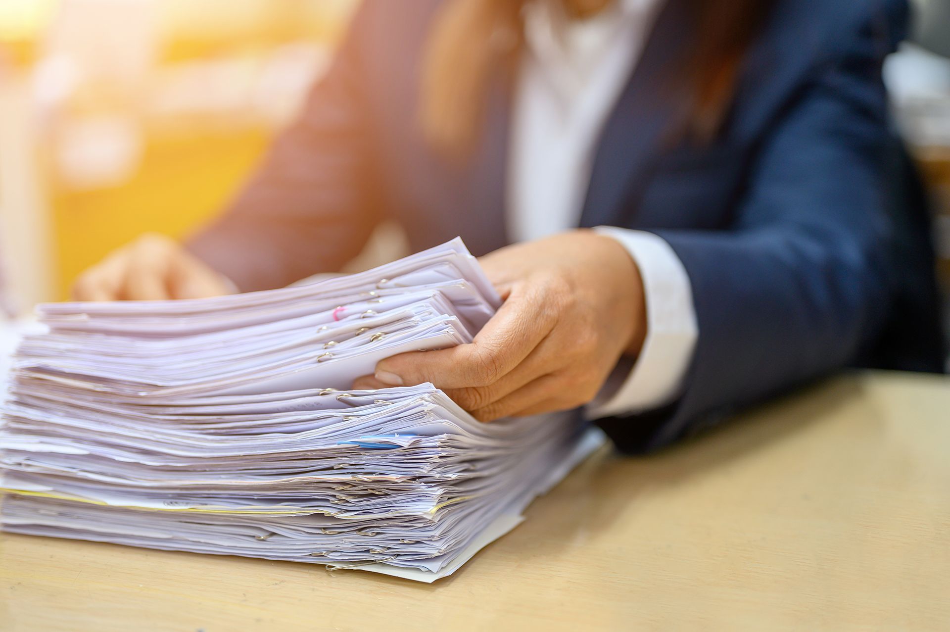 A woman is sitting at a desk holding a stack of papers.
