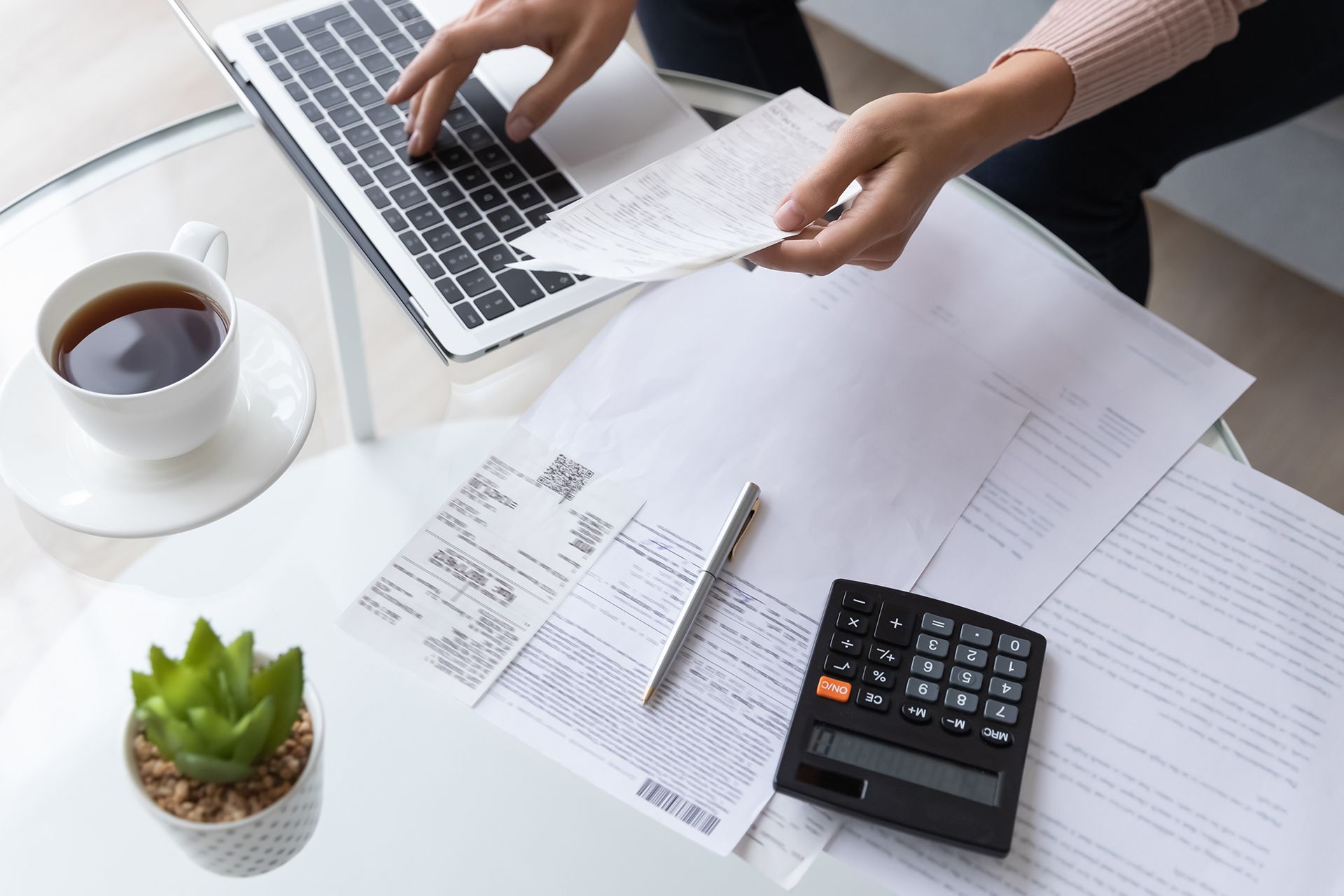A woman is sitting at a desk using a laptop and a calculator.