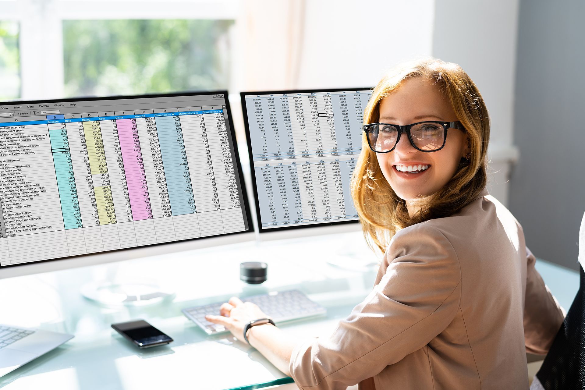 A woman is sitting at a desk in front of two computer monitors.